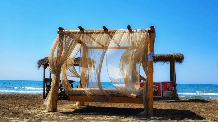 A serene beach scene featuring a bed with a canopy, inviting relaxation under the sun and gentle ocean breeze.