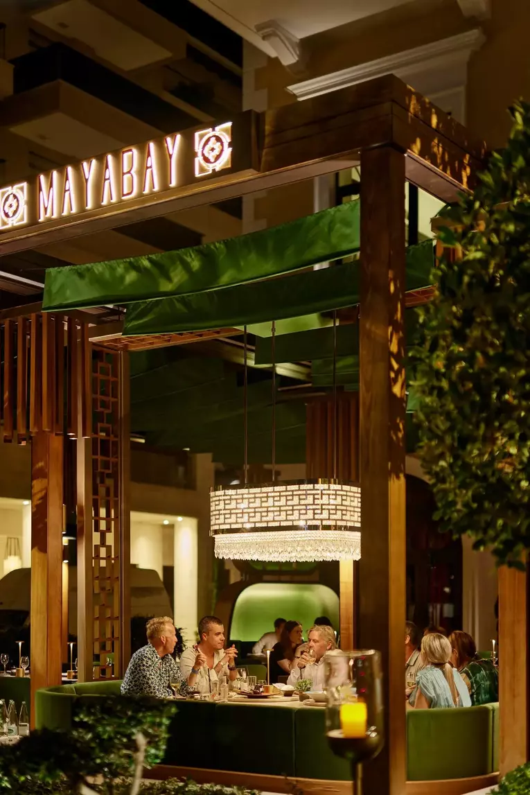 People dining at the elegantly outdoor MayaBay restaurant in Porto Montenegro at night, featuring a green canopy, modern lighting, and an inviting ambiance.